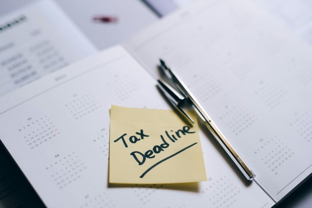 A close-up of a calendar with a sticky note reminding about the tax deadline.